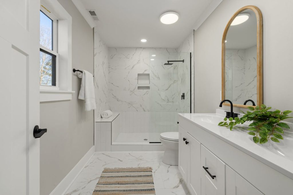Bright modern bathroom featuring marble shower, large mirror, and sleek faucets