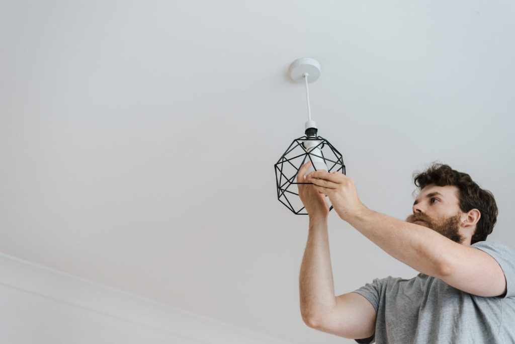 a-person-installing-a-light-bulb-into-a-geometric-pendant-light-fixture-on-the-ceiling