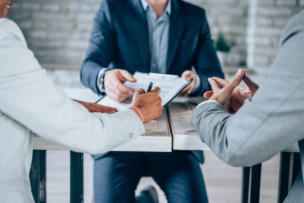 =Shot of three business persons filling in paperwork in an office. Business persons signing a document in board room.