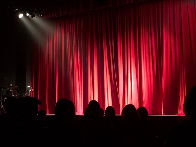 People at a theater with a red curtain across the stage