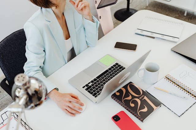 Person sitting at a desk with a laptop, phone, day planner, and phone