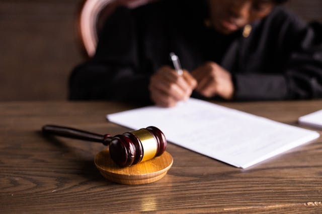 A gavel resting on a desk with a person blurred out in the background signing papers