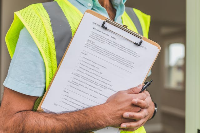 Person wearing a yellow safety vest, holding a clipboard with a home inspection checklist attached to it