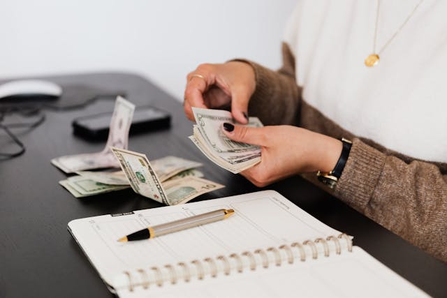 Person counting money in both hands beside a notebook and pen