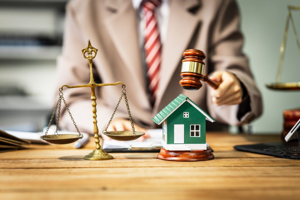 A person holding a gavel over a small figurine of a house
