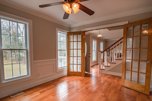 An empty room with a ceiling fan and large windows.